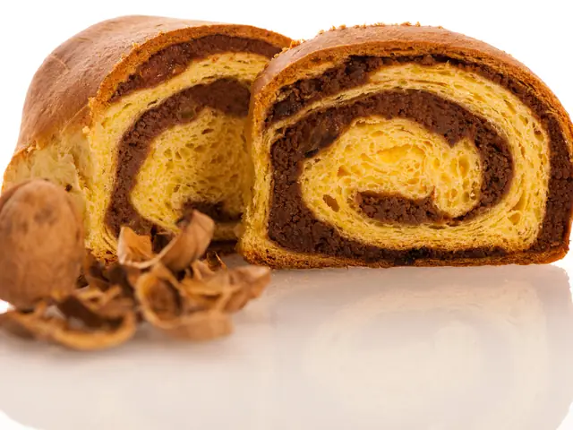 Cozonac cu nucă tăiat în două, cu spirala de umplutură de nucă și cacao la vedere, lângă o nucă și coji