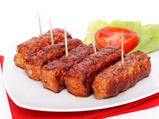 Mici rumeniți pe farfurie albă, cu roșie și salată verde alături