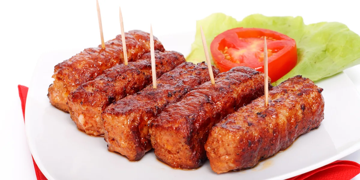 Mici rumeniți pe farfurie albă, cu roșie și salată verde alături