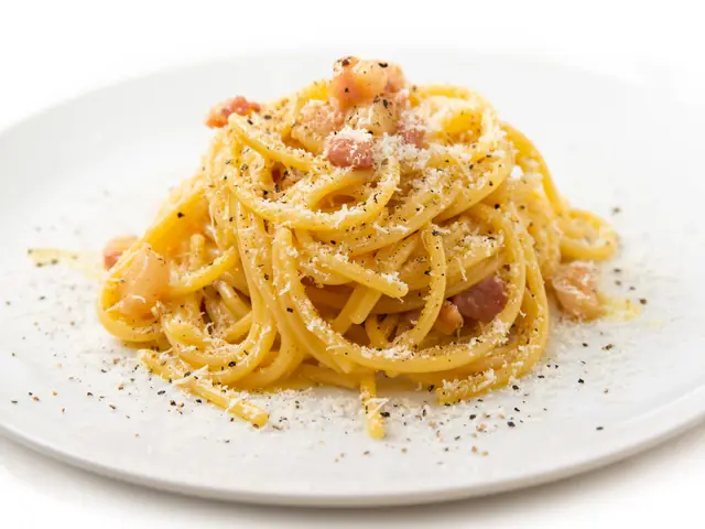 Spaghete carbonara pe o farfurie albă, cu bucăți de guanciale, pecorino ras și piper negru