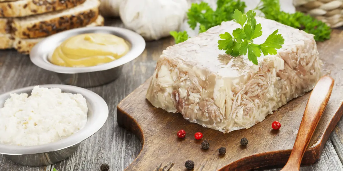 Piftie de porc închegată, întoarsă pe un fund de lemn, cu pătrunjel, boabe de piper, muștar și hrean alături