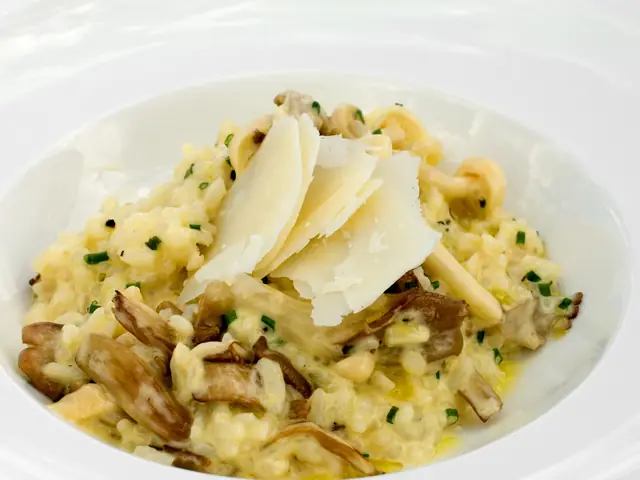 Risotto cremos cu ciuperci, așchii de parmezan și arpagic, într-o farfurie adâncă albă