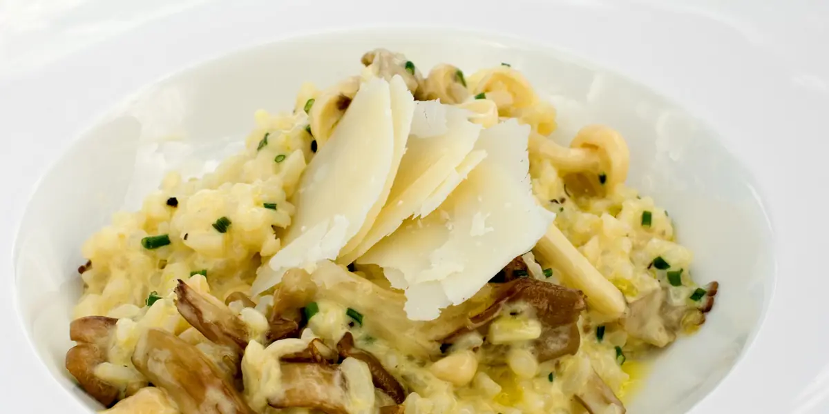 Risotto cremos cu ciuperci, așchii de parmezan și arpagic, într-o farfurie adâncă albă