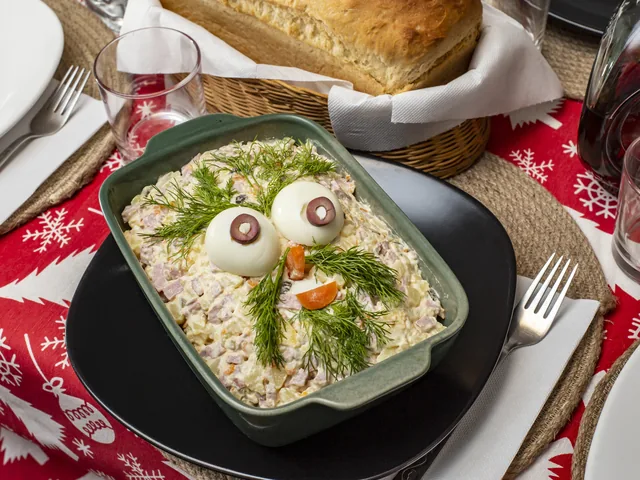 Salată de boeuf într-un vas de ceramică, decorată cu ouă fierte și mărar, pe o masă de Crăciun