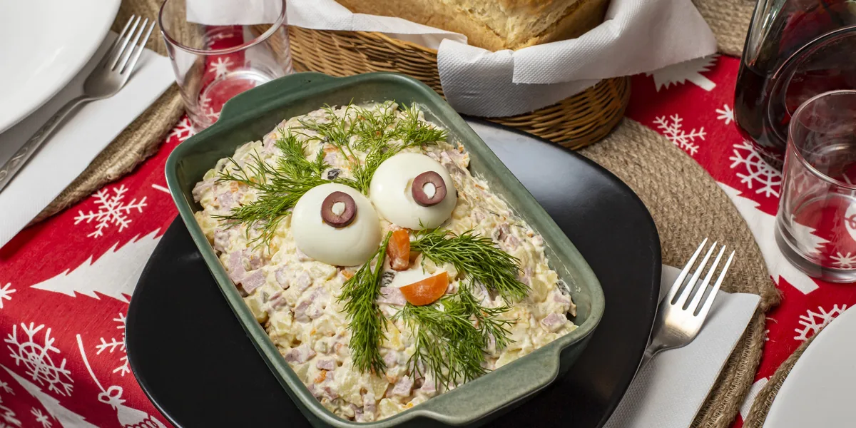 Salată de boeuf într-un vas de ceramică, decorată cu ouă fierte și mărar, pe o masă de Crăciun